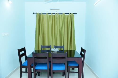 a dining room table with blue chairs and a green curtain at Athrakkattu Enclave in Trivandrum