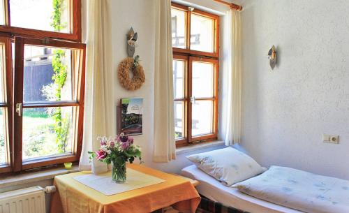 a room with a table and a bed and two windows at Berghof Lichtenhain in Lichtenhain