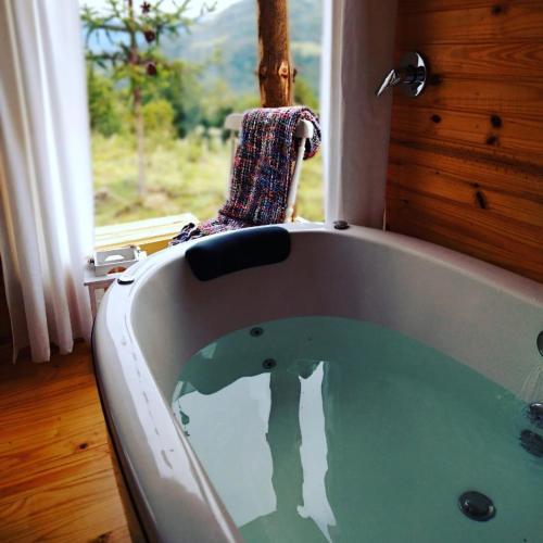 a bath tub in a room with a window at Cabana Refúgio - Pousada Colina dos Ventos in Urubici