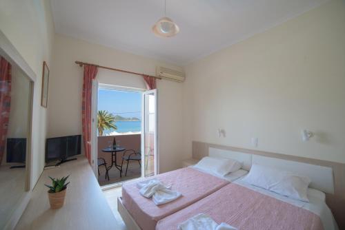 a bedroom with a pink bed and a balcony at Alkyon Beach Hotel in Agios Georgios Pagon