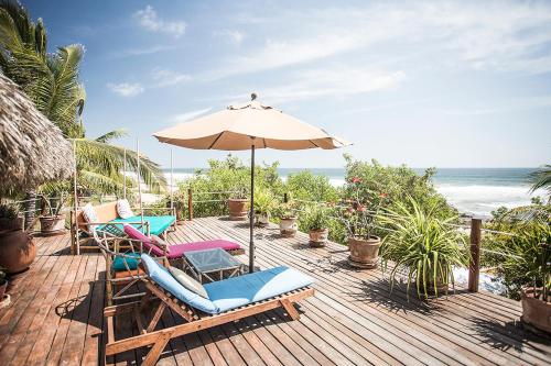 a deck with chairs and an umbrella and the ocean at Present Moment Retreat in Troncones