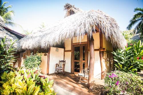 a house with two chairs and a thatched roof at Present Moment Retreat in Troncones