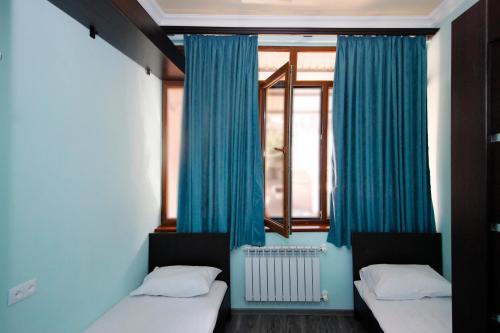 een kamer met 2 bedden en een raam met blauwe gordijnen bij Hotel Victoria in Jerevan