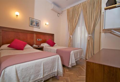 a hotel room with two beds with red pillows at Hostal Greco Gran Vía Madrid in Madrid