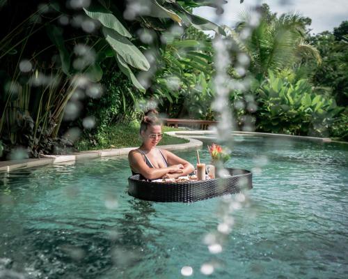 a woman sitting in a swimming pool at Ubud Nyuh Bali Resort & Spa - CHSE Certified in Ubud