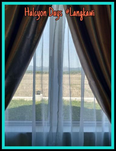 a window with curtains and a view of a field at Halcyon Days @ Langkawi in Pantai Cenang