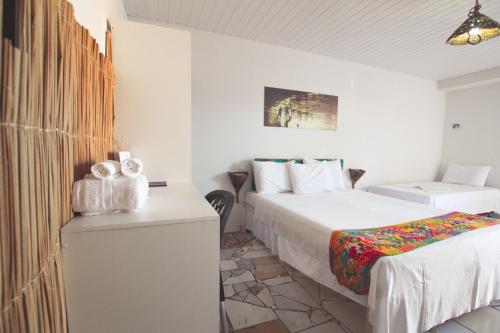 a white room with two beds and a table with a bed sqor at Pousada Vila Nalu in Praia do Frances