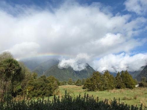 a rainbow in the sky over a mountain range at High Peaks Hotel in Fox Glacier