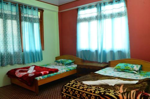 two beds in a room with blue curtains at VAMOOSE PARKHA SIKKIM in Rangli