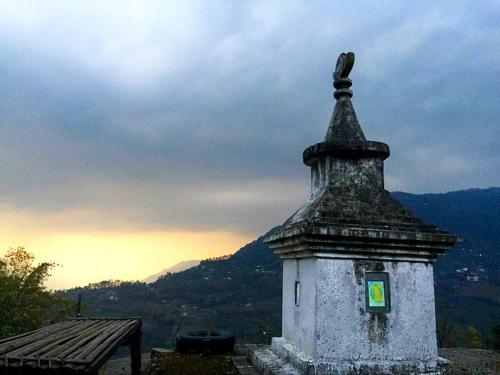 a stone tower with a green sign on it next to a bench at VAMOOSE PARKHA SIKKIM in Rangli