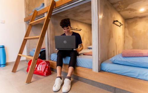 a person sitting on a bed using a laptop in a bunk bed at Jedi Hub Hostel in Limassol