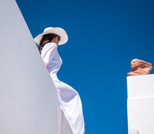 a woman in a hat standing on top of a building at Amelot Art Suites in Fira