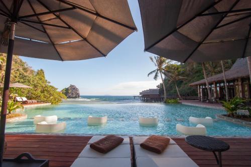 a pool with chairs and an umbrella and the ocean at Cauayan Island Resort and Spa in El Nido