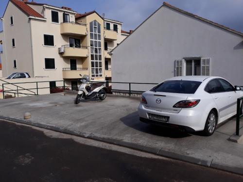a white car parked next to a motorcycle in a parking lot at Rooms Kvestic in Dubrovnik