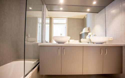 een badkamer met 2 wastafels, een bad en een spiegel bij Hotel Paradisio by WP Hotels in Blankenberge