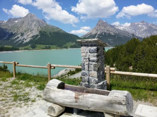 a wooden bench in front of a lake with mountains at Casa Zebrusius - Zebrusius's App in Valfurva