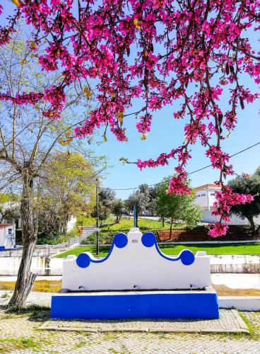 a blue and white bench under a tree with pink flowers at Termas da Sulfurea in Cabeço de Vide