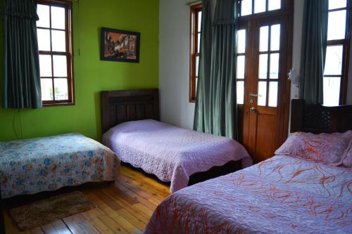 2 camas en una habitación con paredes y ventanas verdes en Hostal del Piamonte, en Quito