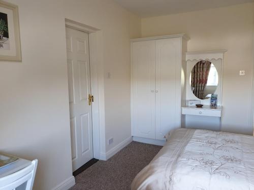 a white bedroom with a bed and a mirror at Glencora B&B in Skibbereen