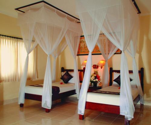 2 Betten mit weißen Vorhängen in einem Schlafzimmer in der Unterkunft Aneka Lovina Villas & Spa in Lovina