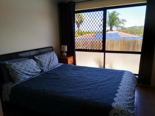 a bedroom with a blue bed and a large window at Cosy, self-contained and central to everywhere in Gold Coast