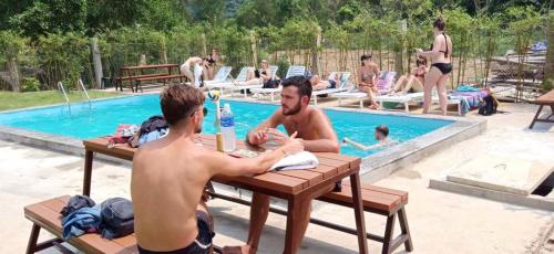 dos hombres sentados en una mesa frente a una piscina en Central Backpackers Hostel - Phong Nha, en Phong Nha