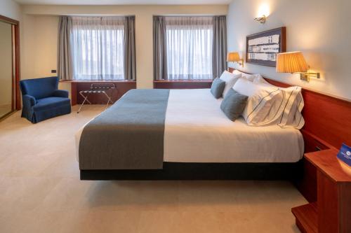 a hotel room with a large bed and a blue chair at Gran Hotel Rey Don Jaime in Castelldefels