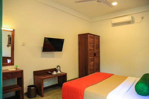 a bedroom with a bed and a desk and a television at Fresco Water Villa in Sigiriya