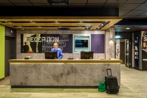 a man standing in front of a counter with a sign on it at ibis budget Berlin Kurfürstendamm in Berlin