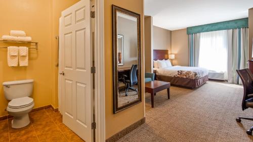 a hotel room with a bed and a toilet and a mirror at Best Western Dothan Inn & Suites in Dothan