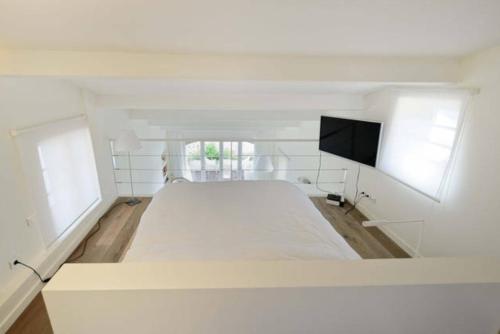 une chambre blanche avec un grand lit et une télévision à écran plat dans l'établissement L’Ile Rousse les pieds dans l’eau, à LʼÎle-Rousse