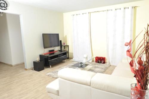 uma sala de estar com um sofá branco e uma televisão em Les Héliconias Résidence cosy et calme em Les Abymes