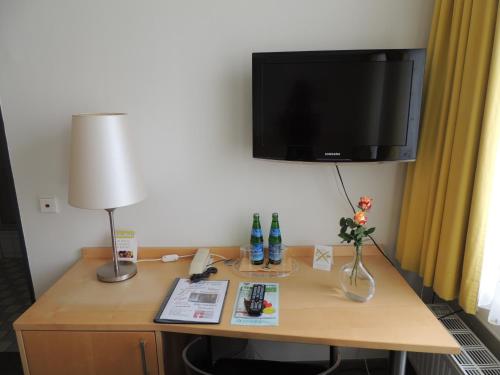 a desk in a hotel room with a tv on the wall at CVJM Düsseldorf Hotel & Tagung in Düsseldorf