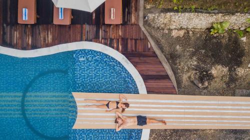 a woman laying on a bench next to a swimming pool at Kabeh Jati Garden Villa & Restaurant in Nusa Penida