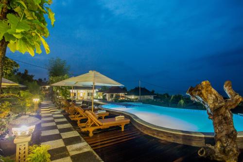 a swimming pool with tables and chairs and an umbrella at Kabeh Jati Garden Villa & Restaurant in Nusa Penida