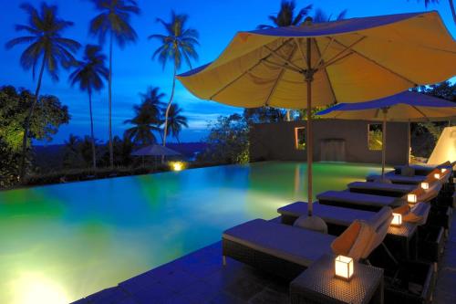 a pool at night with chairs and an umbrella at Kahanda Kanda in Koggala