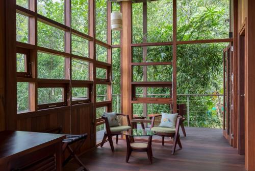 a room with large windows and a table and chairs at Niraamaya Retreats Cardamom Club in Thekkady