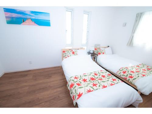 two beds in a room with white walls and windows at Kourijima L'hotels in Nakijin