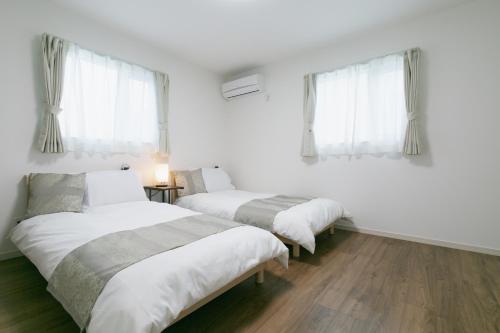 two beds in a room with white walls and windows at Kourijima L'hotels in Nakijin