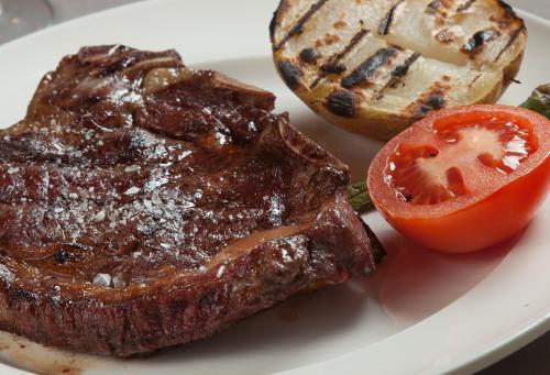 a steak and a tomato on a white plate at Hotel Restaurant Les Brases in Sort