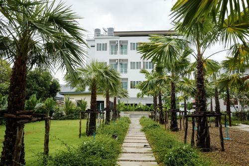 um caminho em frente a um edifício branco com palmeiras em Chez Bure - Bure Homestay em Kanchanaburi