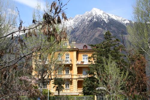 a yellow building with a snow covered mountain in the background at Hotel Villa Westend in Merano