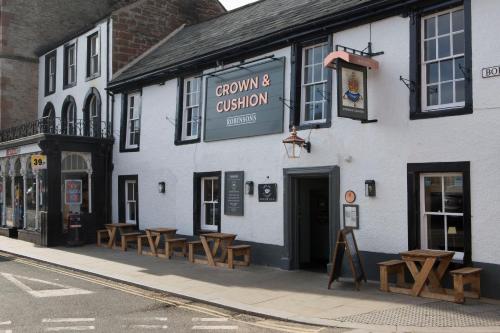 a white building with wooden benches in front of it at Crown and Cushion Appleby in Appleby