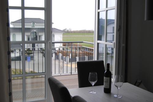 a table with two wine glasses and a view of a balcony at Dünenrose Apartment 7 in Börgerende-Rethwisch