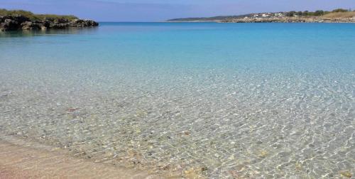 a beach with crystal clear water and a rocky island at Il Giardino delle Jacaranda in Talsano