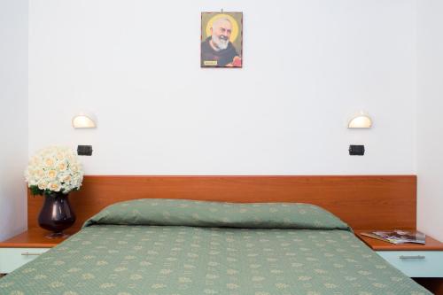 a bed with a green comforter and a picture on the wall at Albergo Villa Marchese in San Giovanni Rotondo