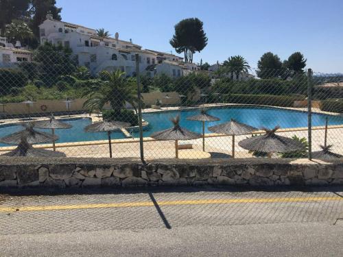 una piscina con sombrillas frente a una valla en Calle Alberca 5, Villotel. Madroñal Urb., 03726 Benitachell,, en Teulada