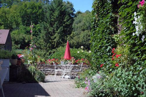 a patio with a red umbrella and chairs and flowers at Gîte la Providence in Saint-Sernin-du-Plain