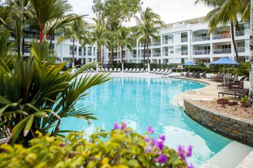 a swimming pool with palm trees and a building at Peppers Beach Club & Spa in Palm Cove