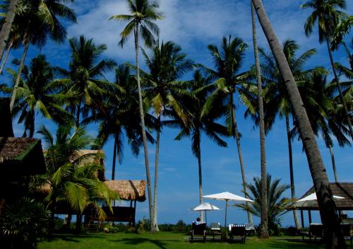 un gruppo di palme con tavoli e ombrelloni di Bon Ton Antique Wooden Villas a Pantai Cenang